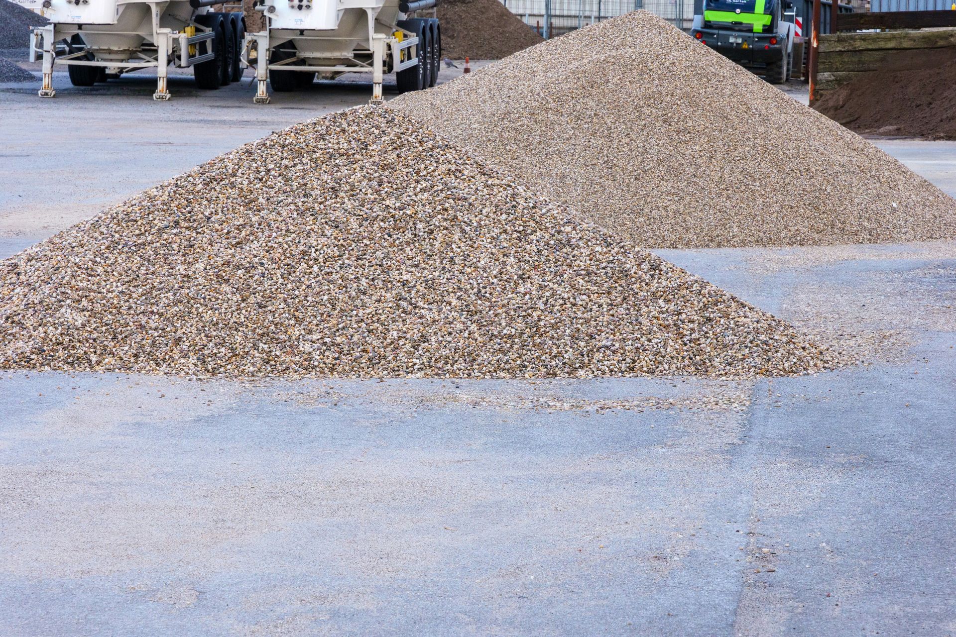 Two large piles of light-colored gravel on concrete pavement